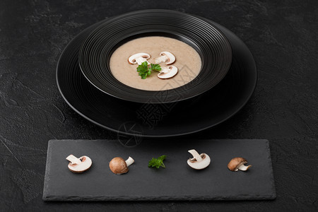黑餐厅盘子底蘑菇汤石板和新鲜蘑菇图片