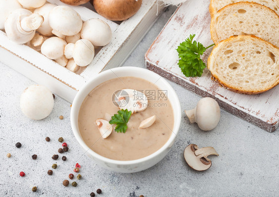 白碗盘的奶油栗椰子辣椒蘑菇汤以浅的厨房背景和一盒生蘑菇新鲜面包为食图片