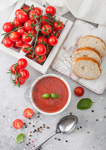 白碗盘的奶油番茄汤匙放在浅底生番茄和面包盒最高视图图片