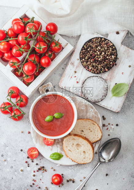 白碗盘的奶油番茄汤匙放在浅底生番茄和面包盒最高视图图片