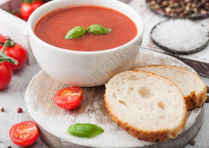 白碗盘的奶油番茄汤匙放在浅底一盒生西红柿和面包图片