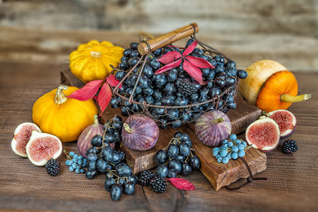 美丽的秋天生命黑葡萄在旧切割板上的篮子中以及成熟的无花果红草莓橙南瓜和木本底有秋叶的黑莓图片