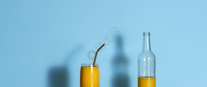 蓝色背景的橙汁和空瓶子玻璃和金属稻草中新鲜挤压的橙汁夏季热带饮料横幅图片