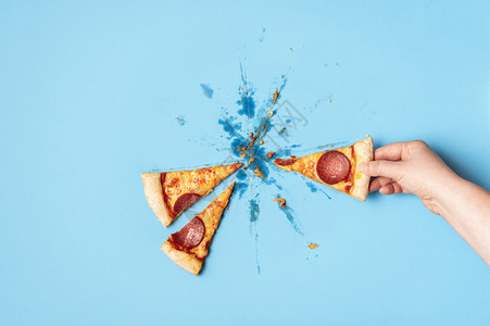 在蓝色背景下吃比萨拉米香肠概念高于女抢一块披萨辣椒抢一块比萨饼不健康的食物饮图片