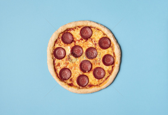 甜美的比萨拉米和融化的奶酪乳和番茄酱在蓝色背景上面可以看到整块辣椒尼比萨饼新鲜的烤披萨图片