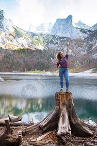 美丽的女孩坐在山湖背景的树桩上图片