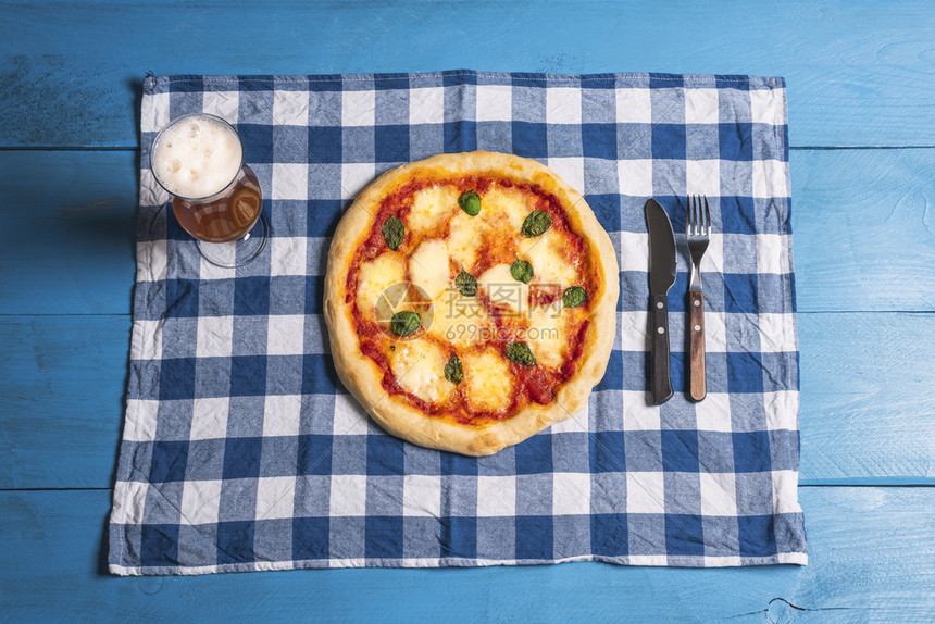 披萨马格赫里塔与熔化的马扎里拉巴西尔和啤酒在巴伐利亚毛巾和蓝色的桌子上面是美味的德国午餐和比萨啤酒图片