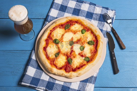 新鲜的比萨玛格丽塔和啤酒在蓝色的巴伐利亚装饰的桌子上花边食物披萨啤酒和蓝餐巾德国的晚融化奶酪比萨图片