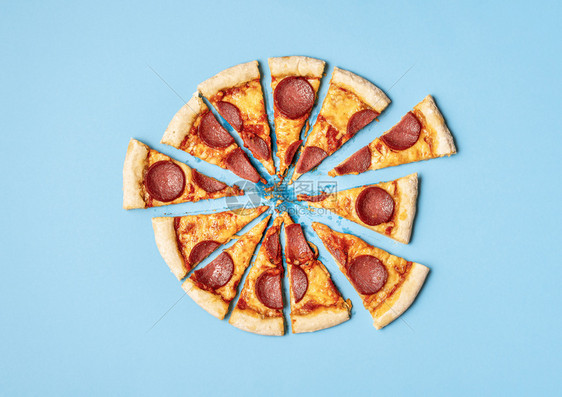 蓝色背景的比萨拉米切成片在的披萨辣椒饼上准备吃披萨快餐不健康的食物美味比萨饼上图片