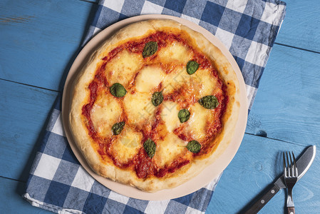 烤盘上的马格赫里塔披萨在巴伐利亚餐巾和蓝桌上鲜烤的马扎瑞拉披萨图片