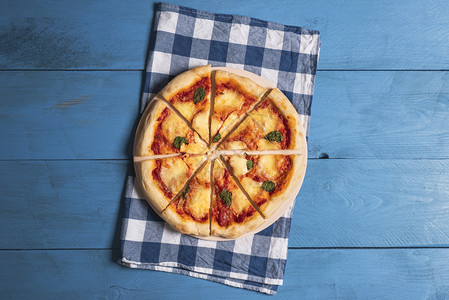 蓝色餐巾纸和木制桌子上的马格赫里塔披萨切片上面是披萨有莫扎里拉和巴西尔准备吃饭的巴伐利亚披萨图片