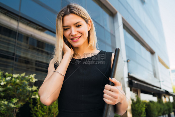 年轻商业妇女站在办公楼外通过电话交谈的肖像商业与成功概念图片