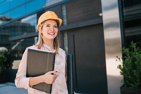 女专业建筑师身着黄头盔的肖像并观看现代建筑室外工程师和概念图片