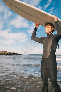 海滩上年轻冲浪手的肖像举起他冲浪板穿着黑色冲浪西装运动和水上的概念图片