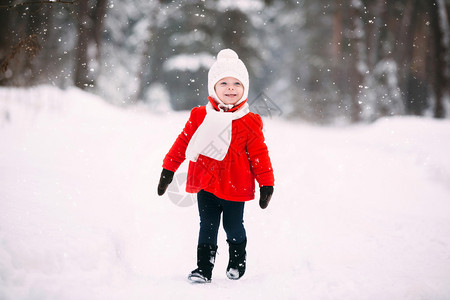 在冬季森林里穿着红大衣的漂亮小女孩冬天玩得开心的小女孩戴着手套和白帽子的快乐小女孩图片