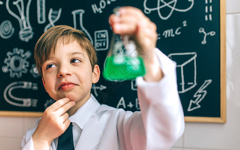 深思熟虑的男孩打扮成化学家酒瓶在黑板前图片