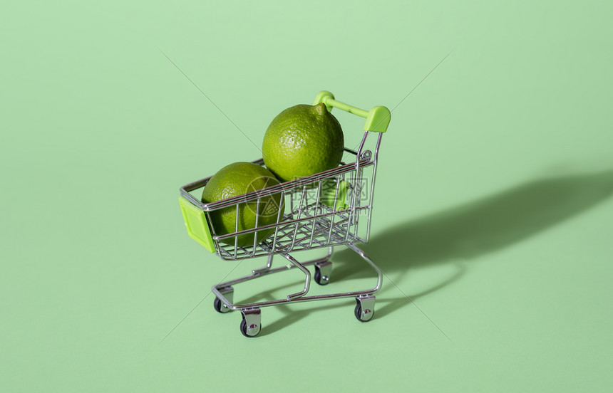 两颗石灰在一辆小型购物车里隔绝在绿色背景上食品购物概念销售购买新鲜水果健康饮食图片