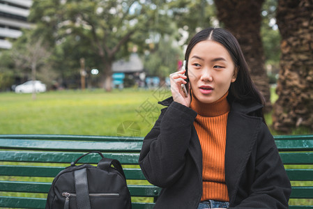 年轻女在公园坐长椅上时电话聊天的肖像图片