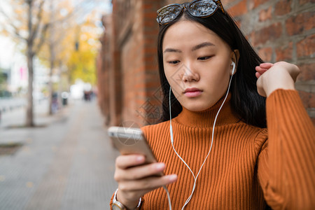 年轻女使用手机与户外耳在街上使用手的肖像图片