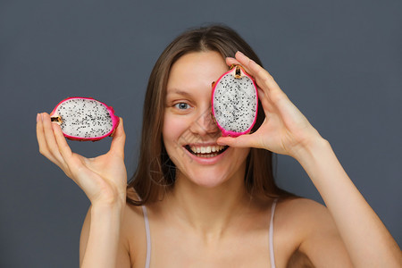 妇女带着热龙果在灰色背景上微笑以或遮住眼睛健康生活方式妇女带着热龙果在灰色背景上微笑图片