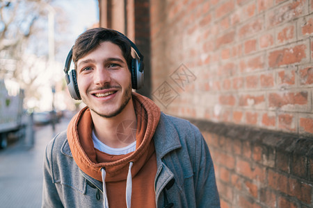 英俊的年轻男子肖像听音乐用耳机对着砖墙城市概念图片