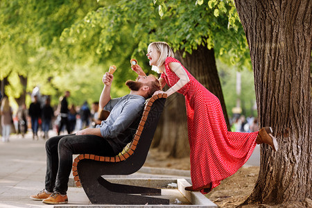 带着胡子的年轻时装男坐在木板凳上金发女郎坐在红衣的长椅上与他一起玩耍带着笑脸的嬉皮男夫妇在城里玩耍和吃冰淇淋带着胡子的年轻时装男图片
