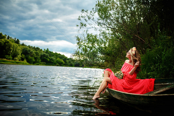 女孩头顶有花圈在河上放轻松和沉睡幻想艺术摄影女美貌的概念自然中休息和水上旅行年轻感女在船上穿红色衣服女孩头上戴花圈在河放松和沉睡图片