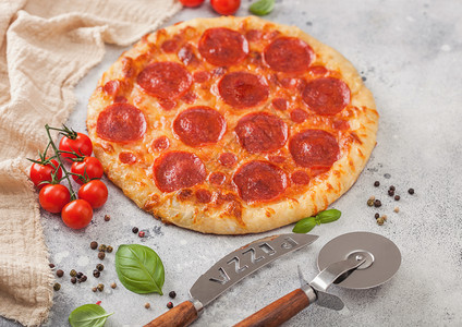 新鲜的圆烤意大利披萨配有切轮刀和子配有西红柿和在轻便厨房餐桌背景上的烤肉图片