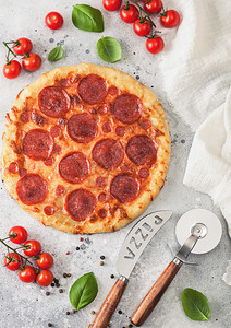 新鲜的圆烤意大利披萨配有切轮刀和子配有西红柿和在轻便厨房餐桌背景上的烤肉图片