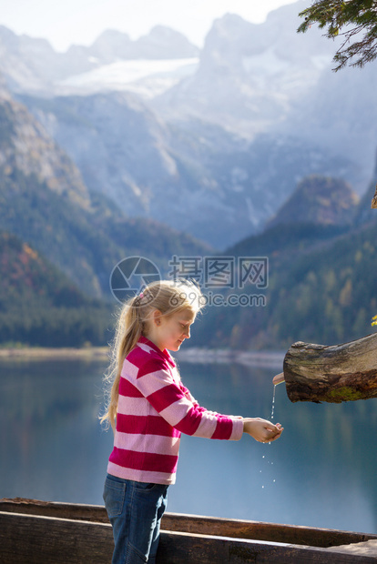 女孩从秋山的木制水沟里喝图片