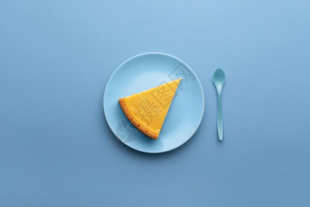 蓝底盘上的一块芝士蛋糕上面是甜点板有芝士蛋糕片和蓝勺子著名的奶酪蛋糕图片