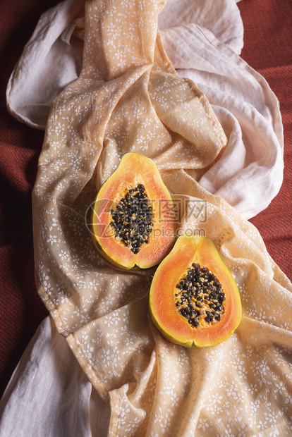 有机木瓜水果切成两半以橙色布料为背景图片