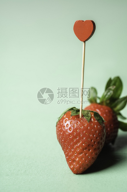 两根草莓和一颗心形牙签夹在其中绿色的无缝背景上成熟的草莓甜美夏日水果情人节卡图片
