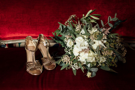 红色经典沙发上的婚嫁花束和金色凉鞋新娘早礼准备红经典沙发上的婚嫁花束和金色凉鞋图片