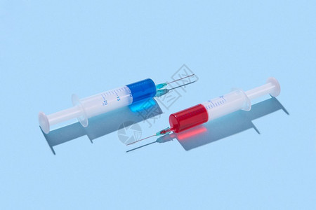 两支手术式一次注射针头20毫升配有红色和蓝血清或注射静脉疫苗在面部蓝底有硬影子复制空间红和蓝色疫苗的塑料注射针筒配有阴影图片