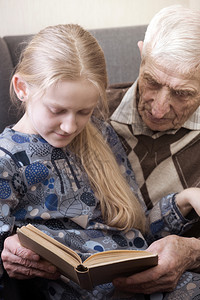 和孙女一起坐在扶手椅上读书的老人肖像图片