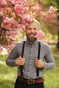 长胡子的人有时髦的发型背景上有樱花穿着紧靠长牙的樱花枝吊带长发与自然概念和谐相处长胡子的人背景上有樱花穿着吊带的长臀人牙齿上有樱图片