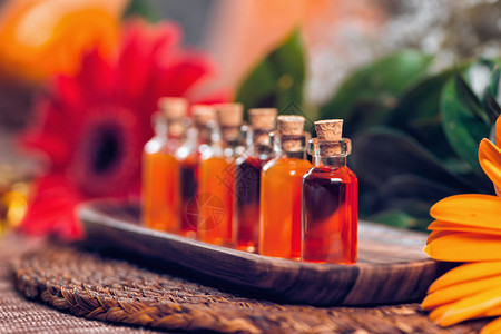 木板上装满红和橙色基本油的透明瓶子红花和油盐灯底芳香疗法放松概念图片