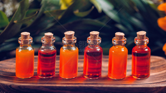 木板上装满红和橙色基本油的透明瓶子图片