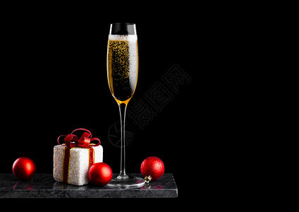 优雅的黄色香槟杯子有气泡圣诞节新年礼物盒和黑底大理石板上的玩具图片
