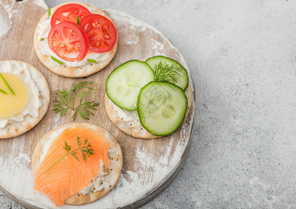 各种圆形健康饼干配有鲑鱼和奶酪西红柿黄瓜在浅色桌底的木切面板上图片