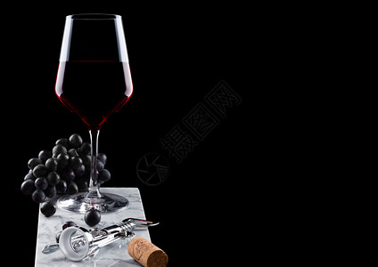 玻璃红葡萄酒大理石板上有深葡萄软木瓶开器和黑底的软木瓶图片