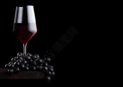 黑色背景的木板上装着深葡萄的优雅红酒杯背景图片