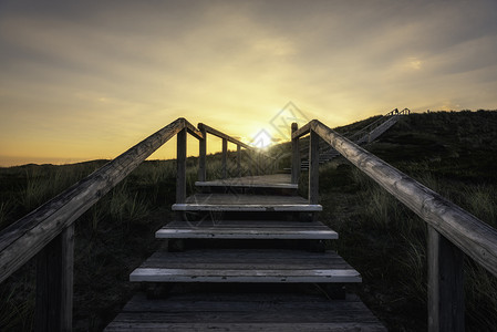 日出时在锡尔特岛的木制楼梯锡尔特海岸线沙丘后面有太阳徒步攀登沙丘图片