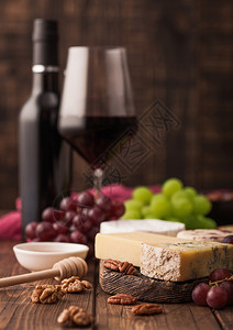 玻璃红葡萄酒和在板上挑选各种奶酪和木制桌底的葡萄图片