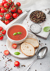 白碗盘的奶油番茄汤匙放在浅底生番茄和面包盒最高视图背景图片