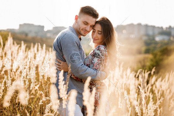 美丽的年轻夫妇拥抱在田野中日落时有草髦的男女在户外玩得开心家庭概念复制空间美丽的年轻夫妇拥抱在日落时有草的田野中图片