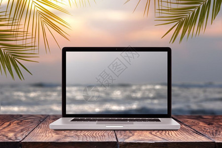 用模糊的海景日出图片在木制桌子上的笔记本显示器以同一背景绿色棕榈叶框复制空间工作于海上办公室外的概念膝上型屏幕模糊的海背景图片