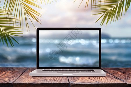 用模糊的海景图显示在木制桌子上以绿色棕榈叶框架为背景复制空间远程在海面岸工作使用办公室外的自然概念笔记本显示带模糊的海面背景图片