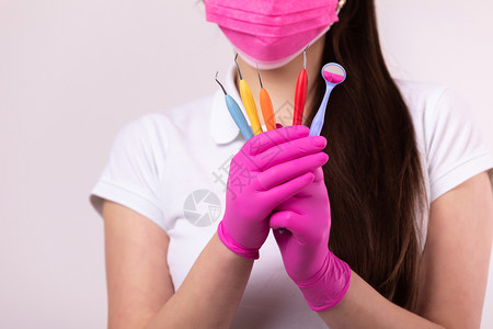 人医药牙科和保健概念穿粉红色面罩的牙医妇女白底带彩色工具的医疗手套图片